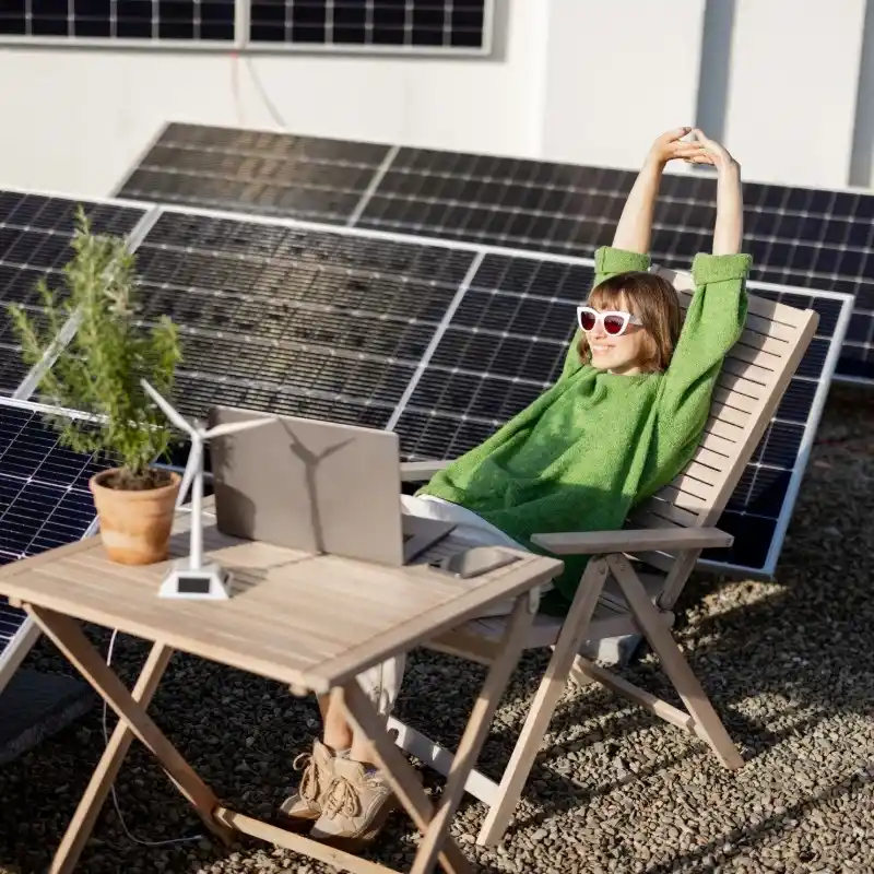 mujer rodeada de placas solares sentada en una silla frente a un ordenador - casa sostenible